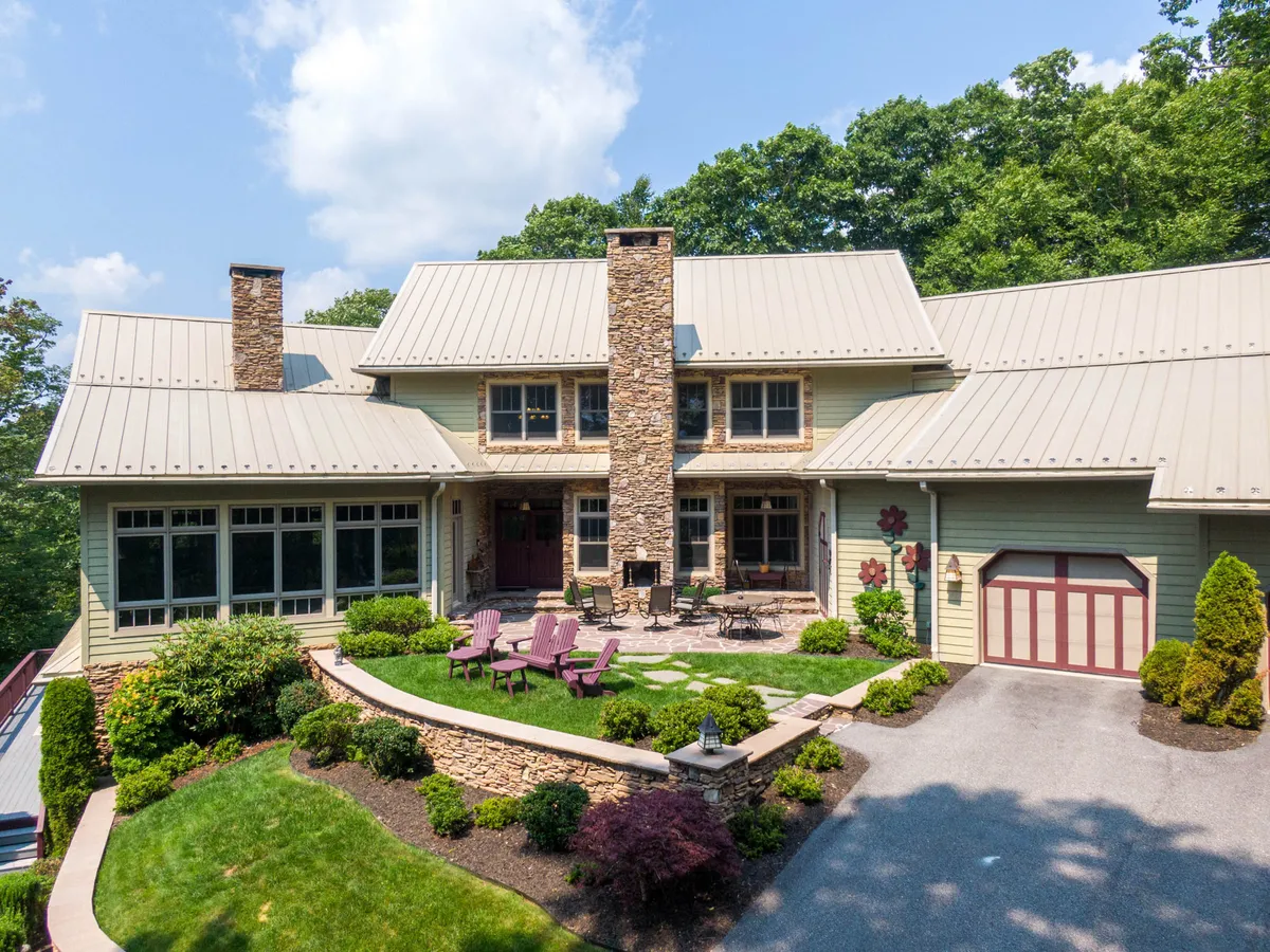 The photo showcases a charming front porch with a stone chimney, landscaped gardens, and a cozy seating area. It's an inviting space that encourages relaxation, outdoor conversations, and enjoying the natural surroundings with friends or family.