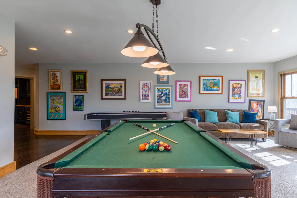 A cozy interior arrangement with a pool table at its center, surrounded by comfortable seating and artwork-adorned walls. This space encourages playful competition and relaxed movie nights alike.
