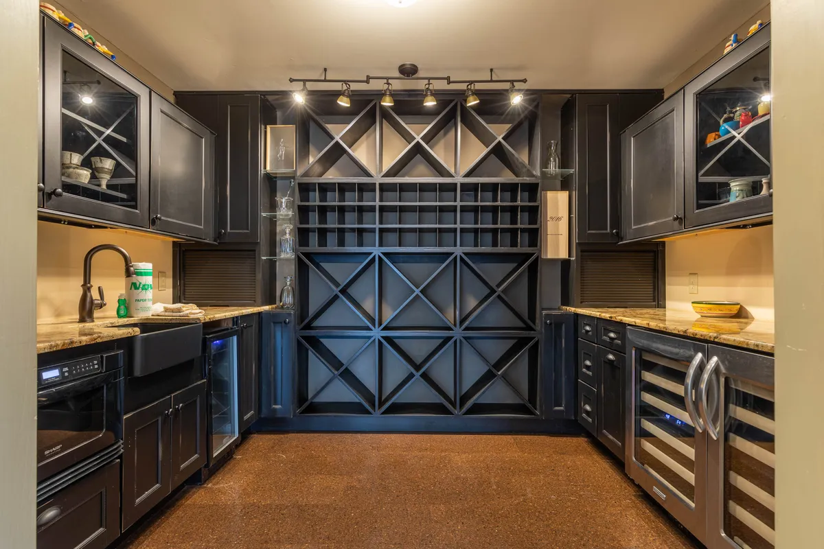 A stylish wine cellar setup featuring sleek black cabinetry, an ample wine storage rack, a granite countertop, and stainless steel appliances. The atmosphere is elegant and intimate, perfect for tastings or celebratory toasts.