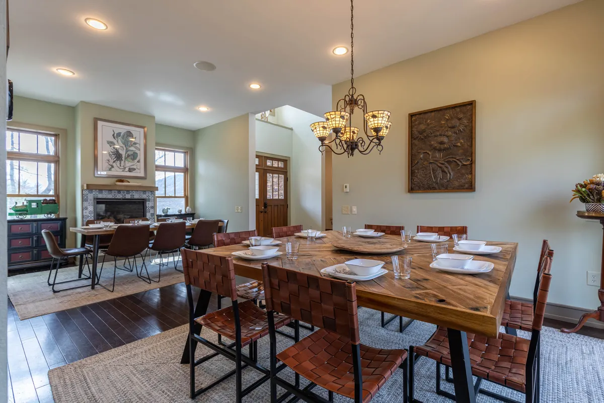 A warm dining space with a large wooden table set beneath a chandelier, accented by artwork and a fireplace. The setting exudes intimacy and comfort, ideal for family dinners, holiday celebrations, or sharing a meal with friends.