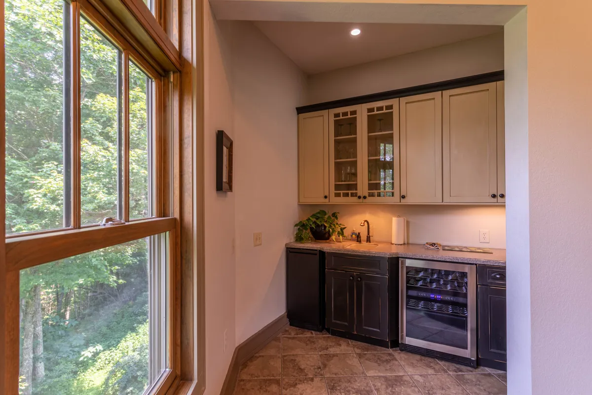 A view of the kitchen area emphasizing elegant cabinetry, a roomy countertop, wine cooler, and a window with a lovely view, suggesting a butler’s pantry or wet bar nearby. The design blends practicality with style, ideal for hosting and entertaining.