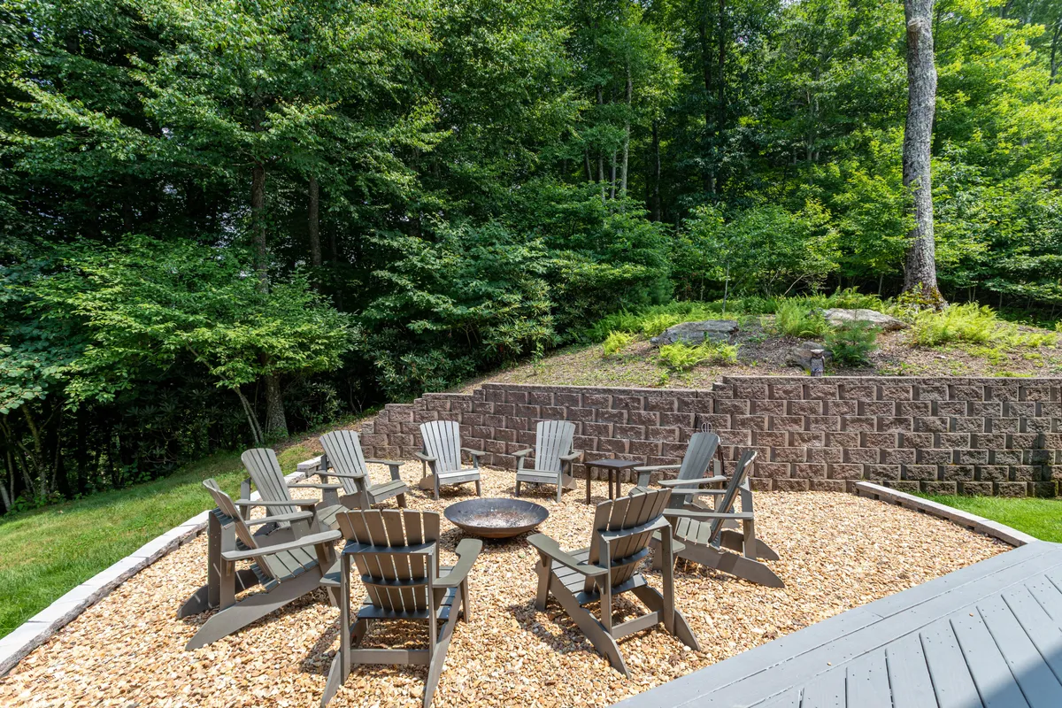 An inviting fire pit surrounded by Adirondack chairs and natural greenery, creating a cozy setting for storytelling, s'mores, or stargazing with friends and family.