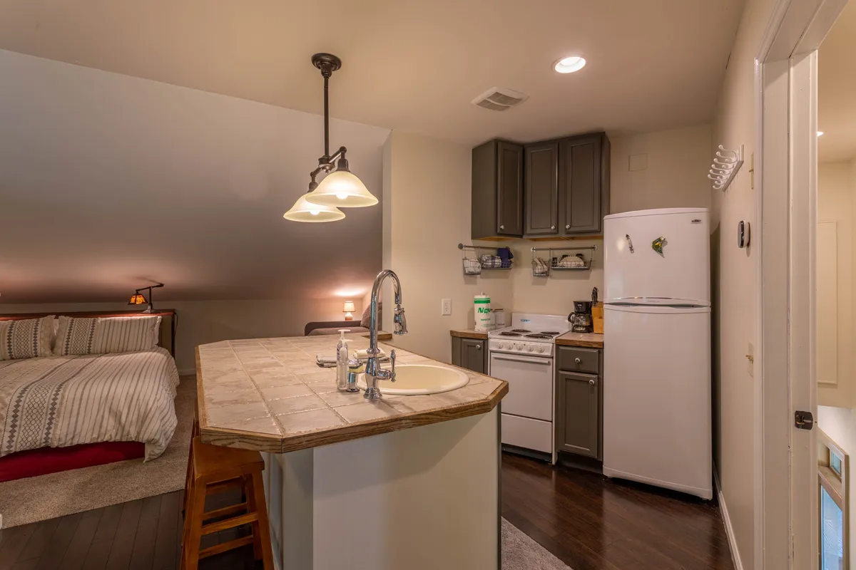 A modern suite with a kitchen island and a bed area in view, highlighted by tasteful lighting fixtures. The open layout suggests a self-contained, comfortable living space ideal for privacy and quiet relaxation.