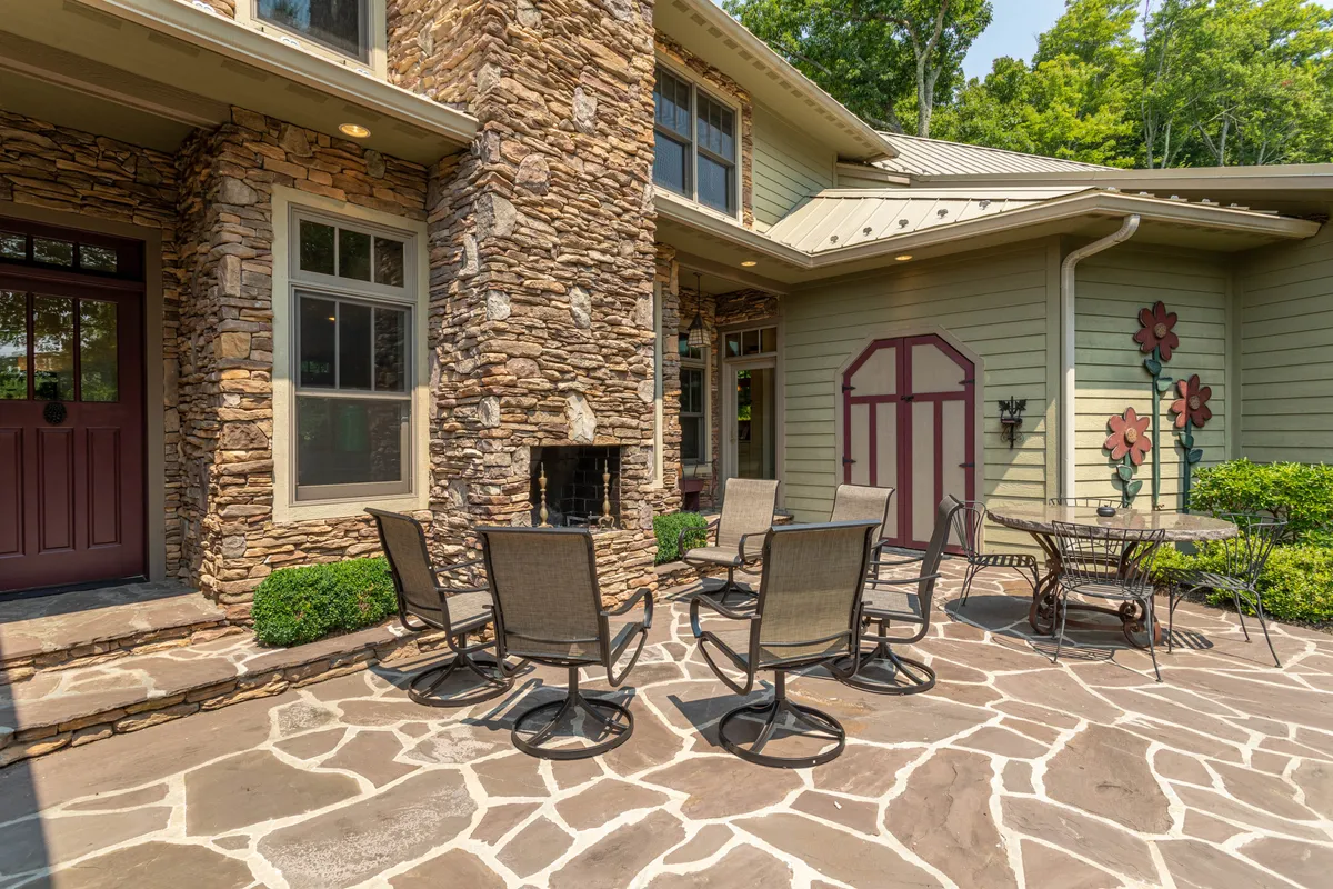 A welcoming patio with a stone woodburning fireplace, outdoor seating area, decorative flowers, and patio flooring. The space feels perfect for cozy evenings, sunset dinners, or morning coffee surrounded by nature.