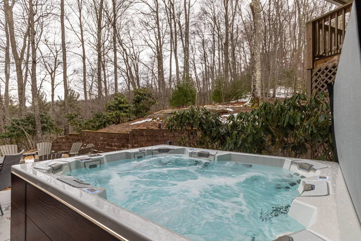 This image captures a serene outdoor patio featuring a private hot tub surrounded by lush trees and comfortable seating. The vantage point offers a sweeping view of the mountains, ideal for relaxation and stargazing. The inviting setting is perfect for unwinding after a day of mountain exploration or luxury shopping nearby.