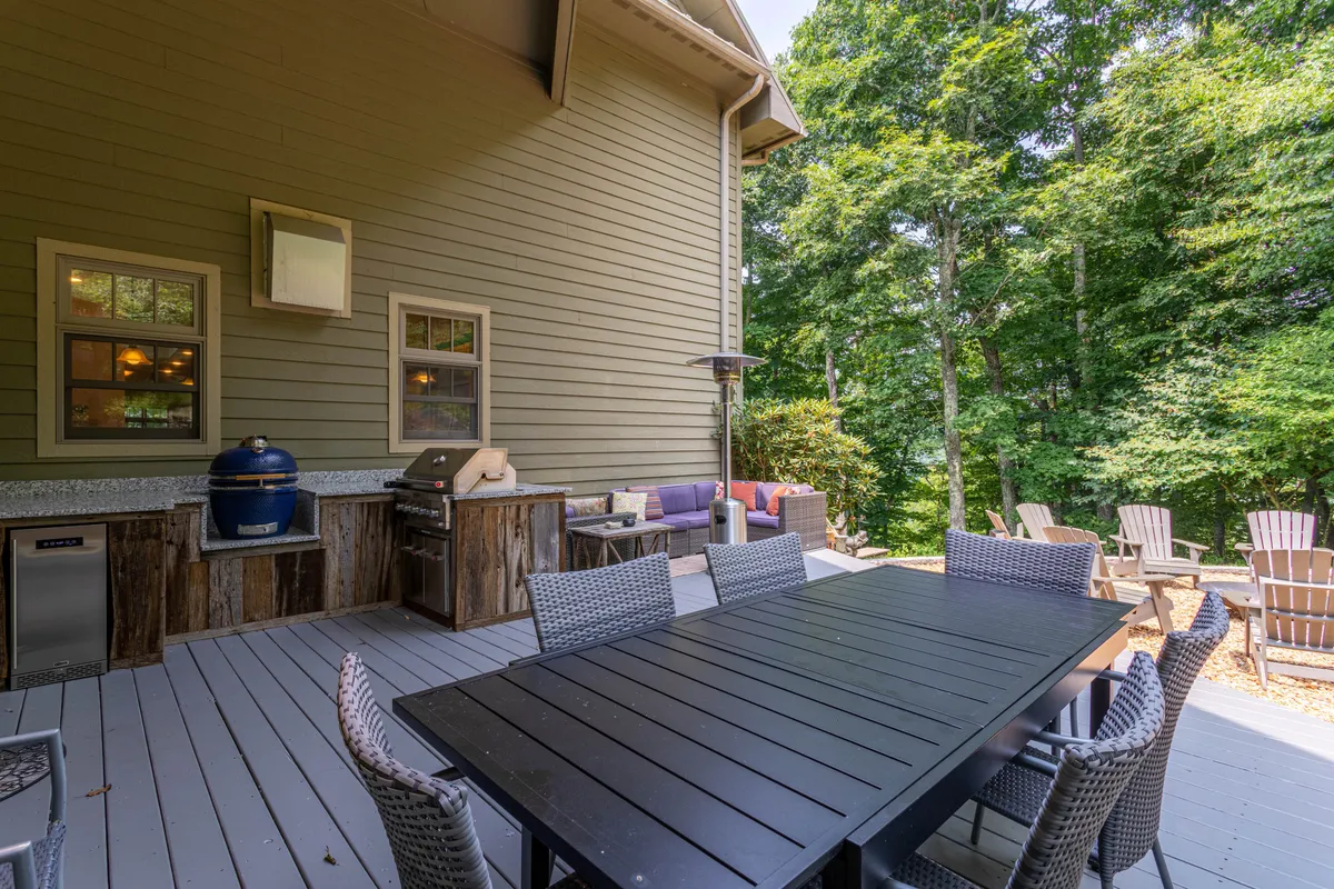 This image captures a spacious outdoor dining area featuring a large table, a grill station, and comfortable seating surrounded by lush greenery. The inviting setup is ideal for groups to gather for alfresco meals, barbecues, or casual conversations while enjoying the fresh mountain air.